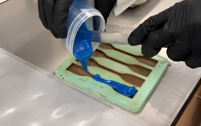 Chemist pouring blue resin into a specimen mold in a testing lab.